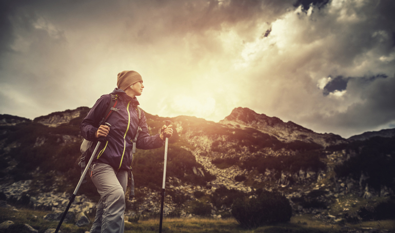 Dame som går på fjellet med sollys på seg gjennom skyene